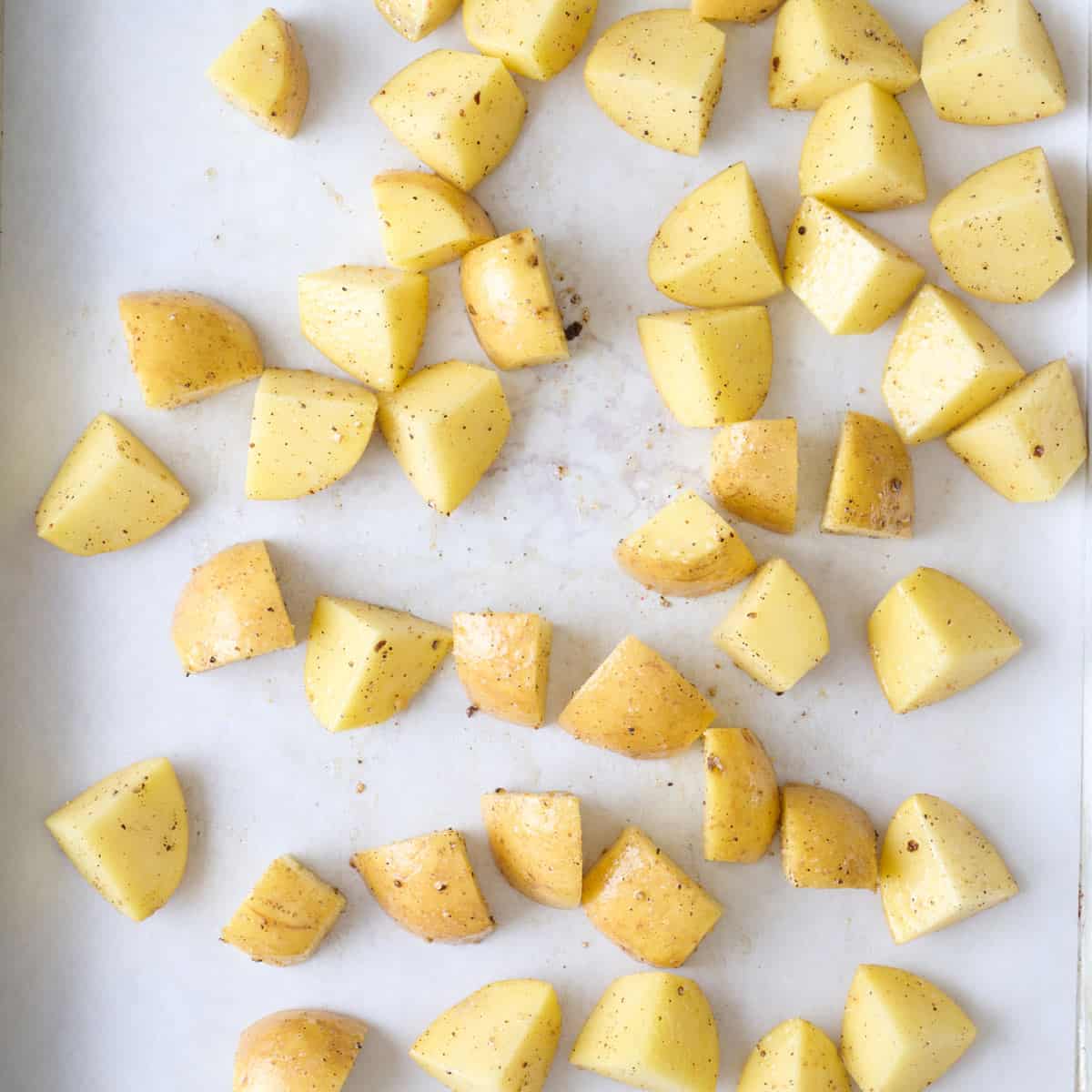 Diced potatoes on a parchment lined sheet pan before roasting.