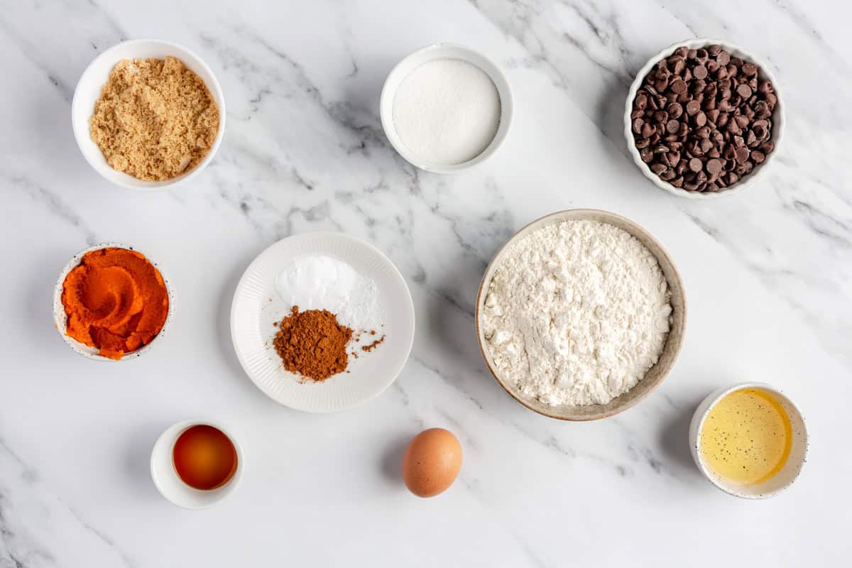 Ingredients for recipe before prepping: brown sugar, white sugar, pumpkin, vanilla, flour, baking powder, baking soda, egg, oil, and chocolate chips.