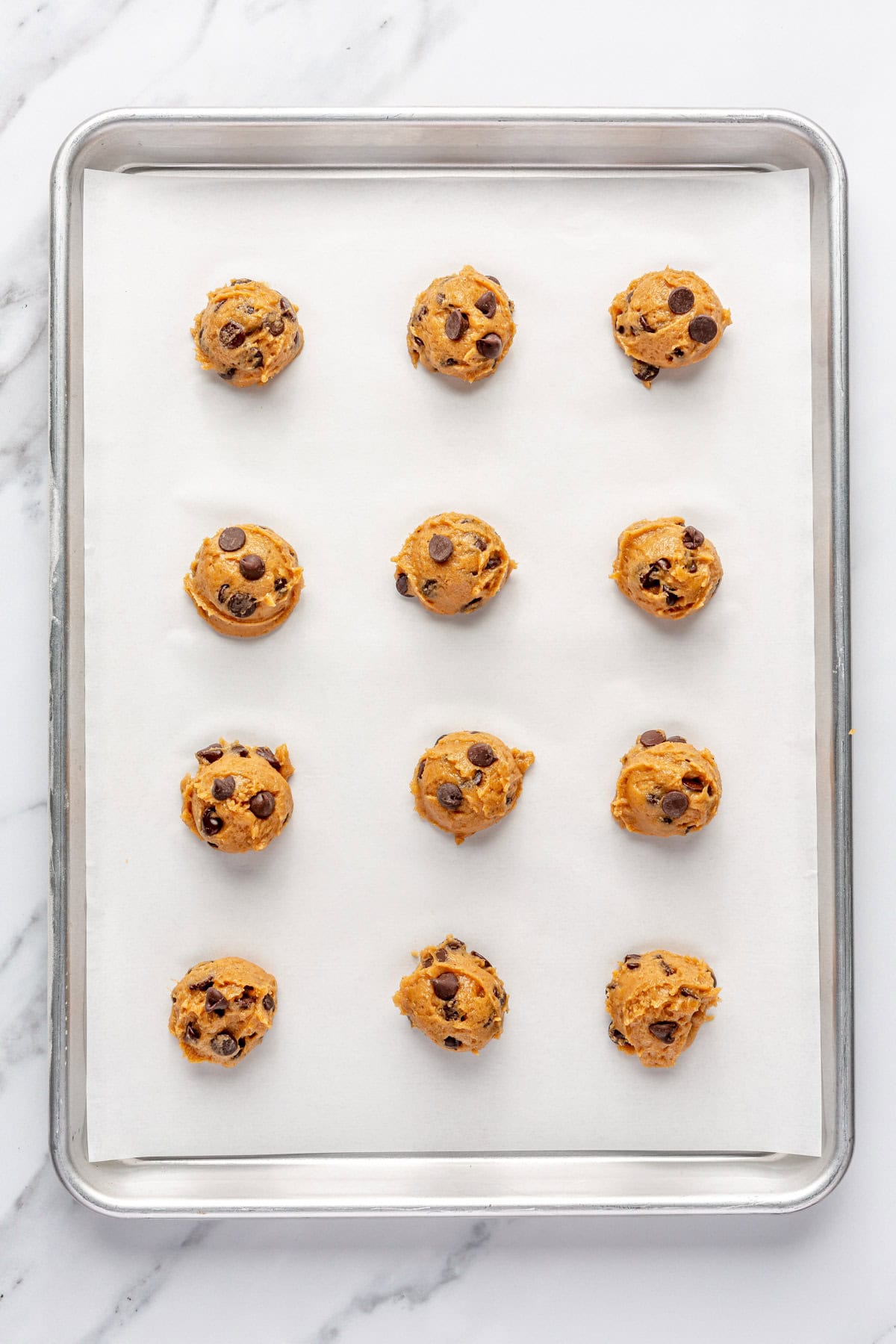 Cookie dough balls on a parchment line baking sheet before baking.