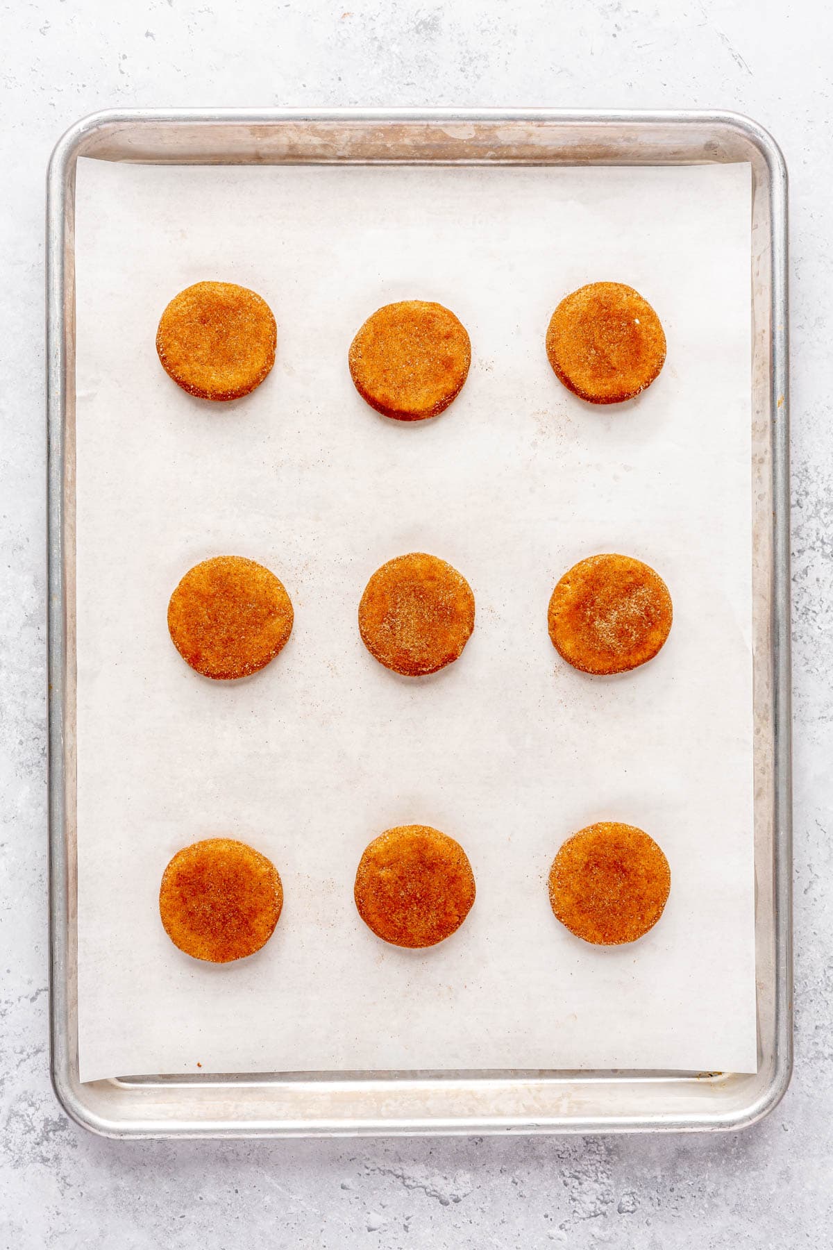 Sugar coated cookie dough balls on a parchment line baking sheet after flattening.