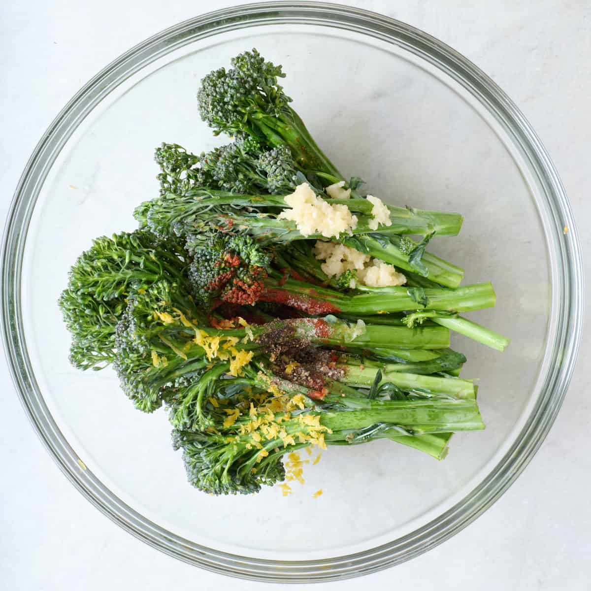 Broccolini in a bowl with garlic, oil and spices.