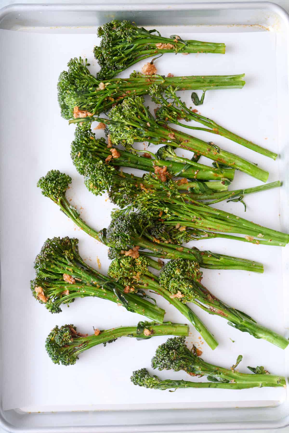 Seasoned broccolini on a parchment lined sheet pan before roasting.