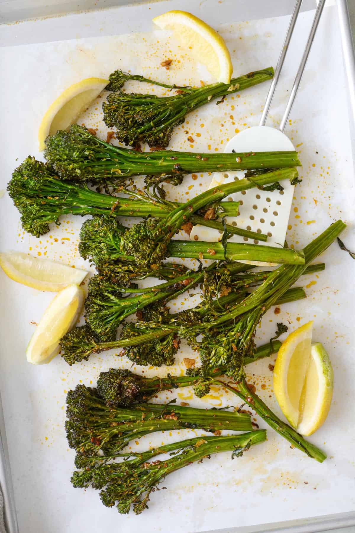 Roasted broccolini on a sheet pan with lemon wedges and spatula.