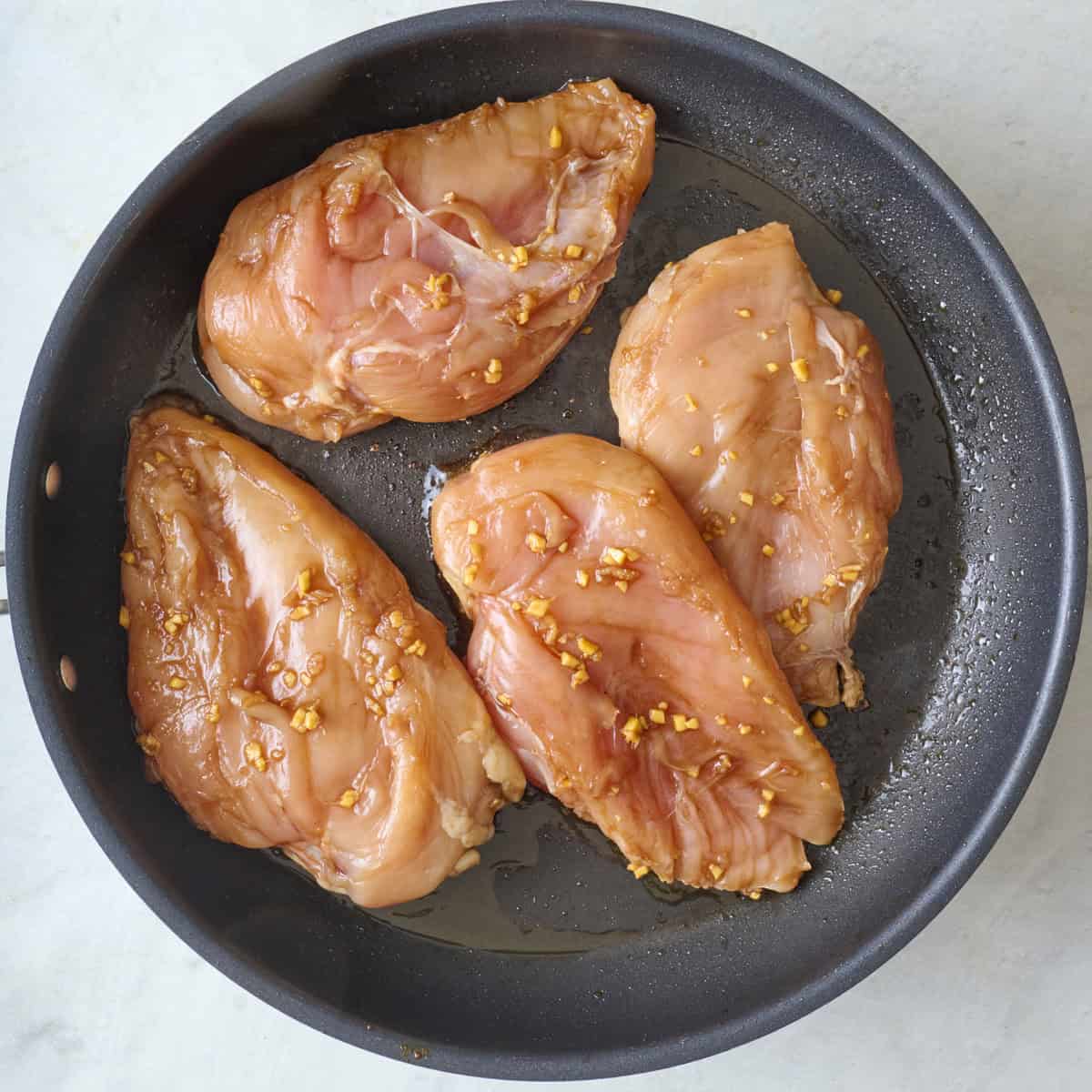 Teriyaki marinated chicken breasts in a skillet before cooking.