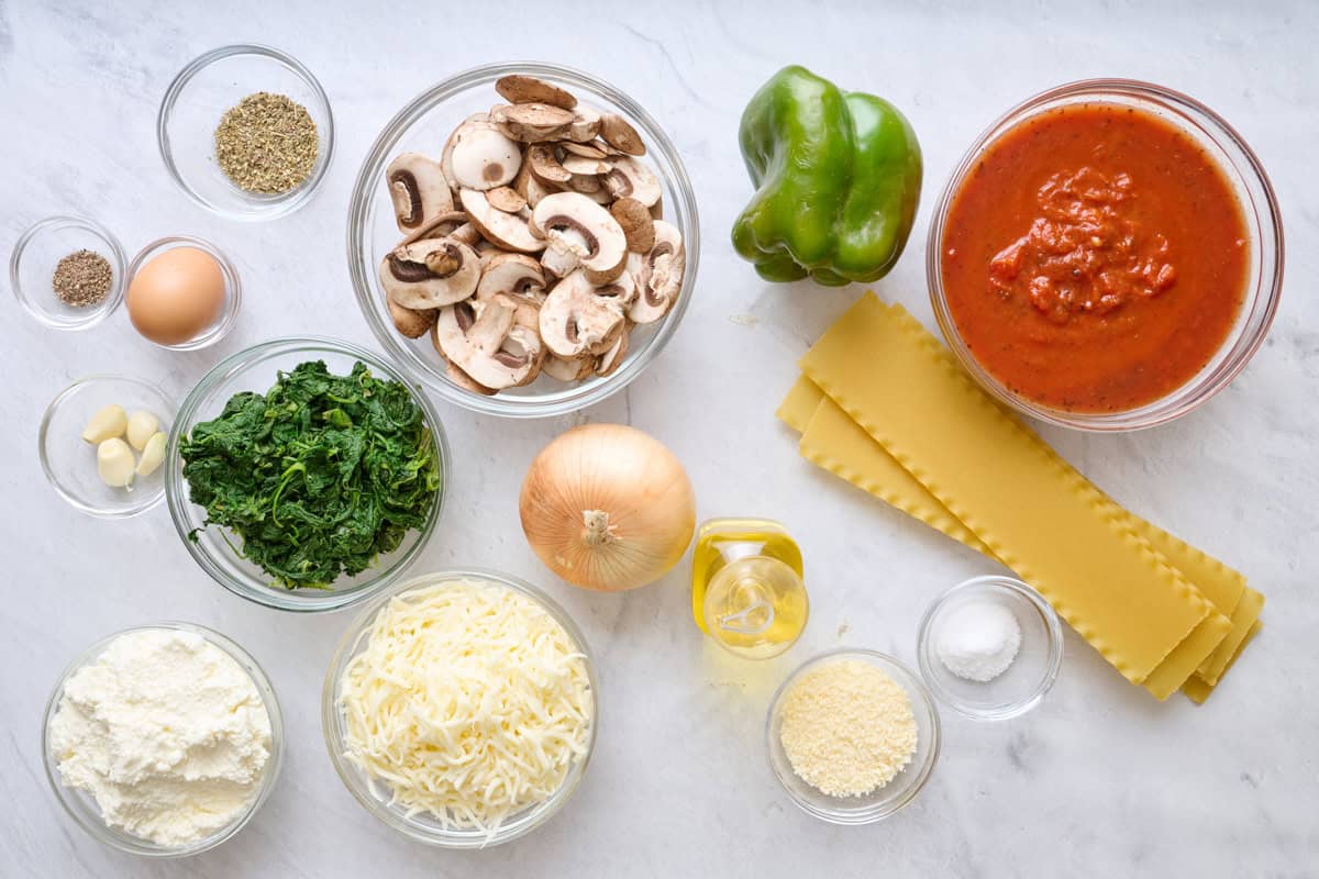 Ingredients for recipe: pepper, egg, garlic cloves, ricotta, shredded mozzarella, spinach, Italian seasoning, sliced mushrooms, onion, green bell pepper, oil parmesan cheese, lasagna sheets, and marinara sauce.