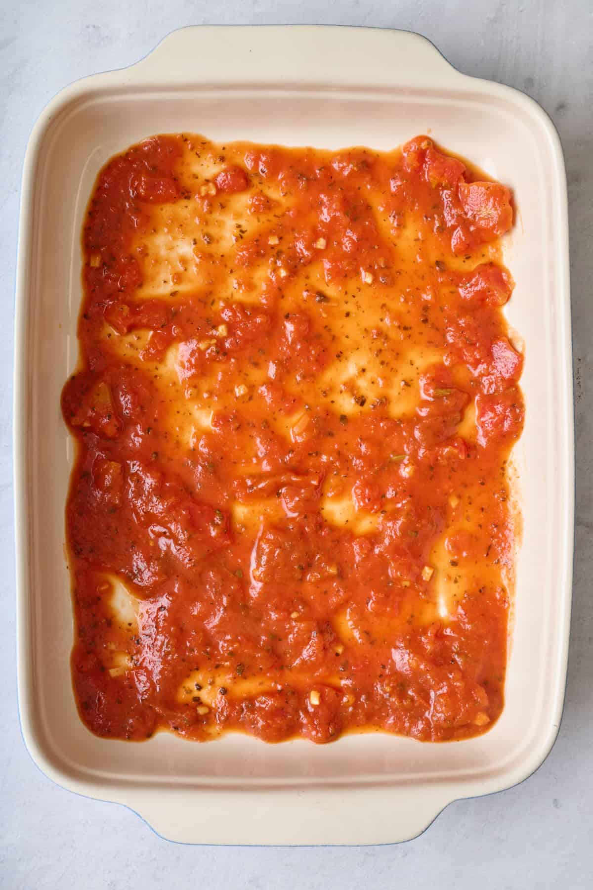 Marinara sauce spread evenly on the bottom of a baking dish.