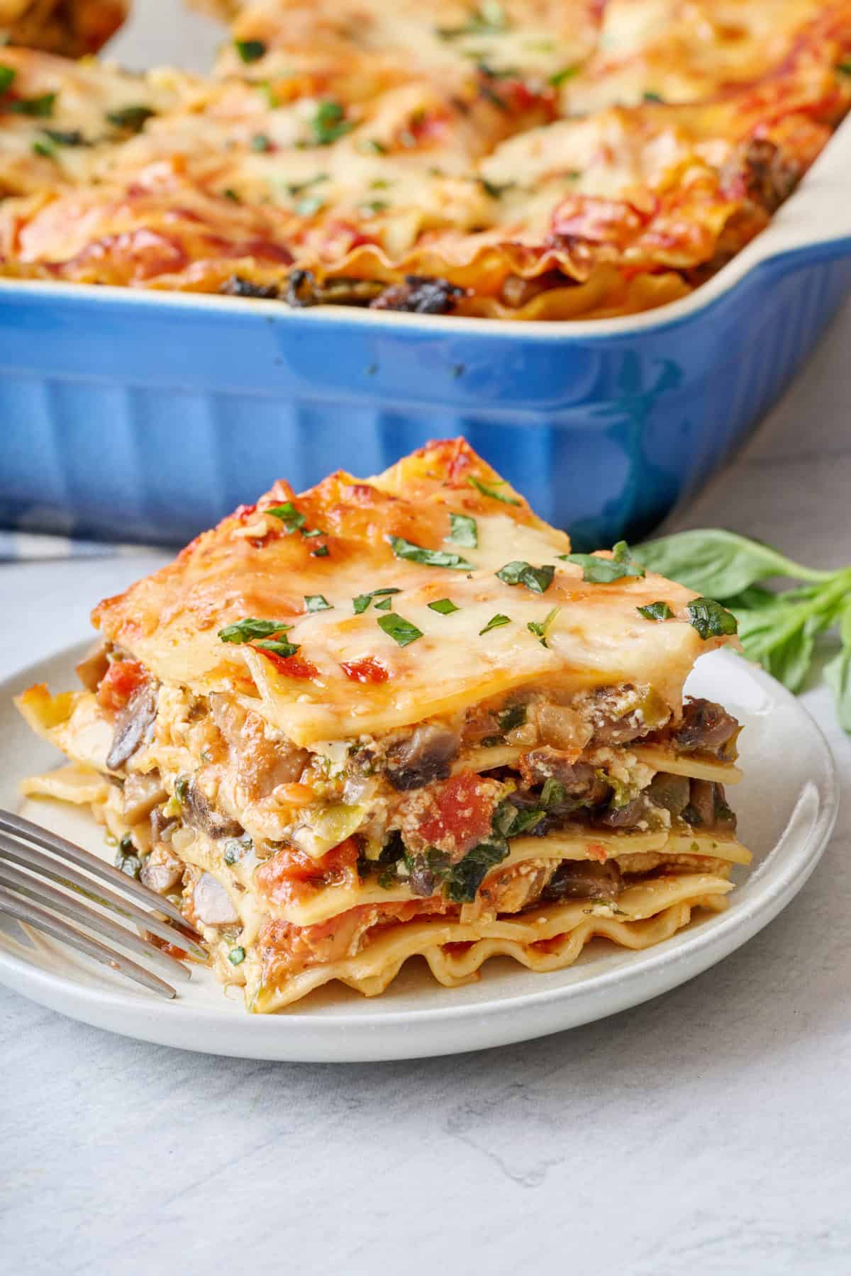 Serving of veggie lasagna on a plate showing each layer with baking dish nearby.