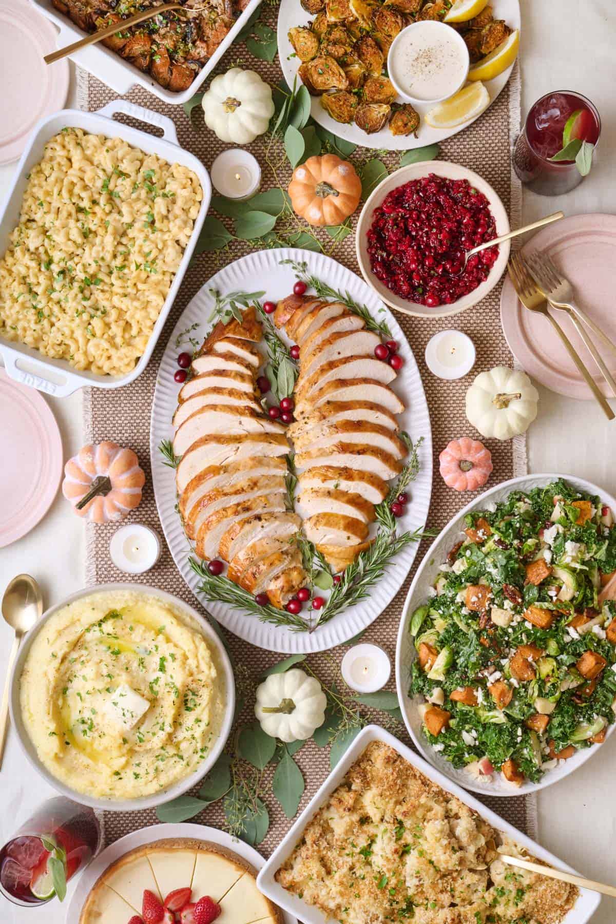 Feel Good Foodie's 2024 Thanksgiving Dinner menu recipes on table including air fryer turkey breast, mashed potatoes, mac and cheese, mushroom stuffing, brussel sprouts, fall harvest salad, cauliflower au gratin, cheesecake cranberry salsa, and pomegranate mocktail.