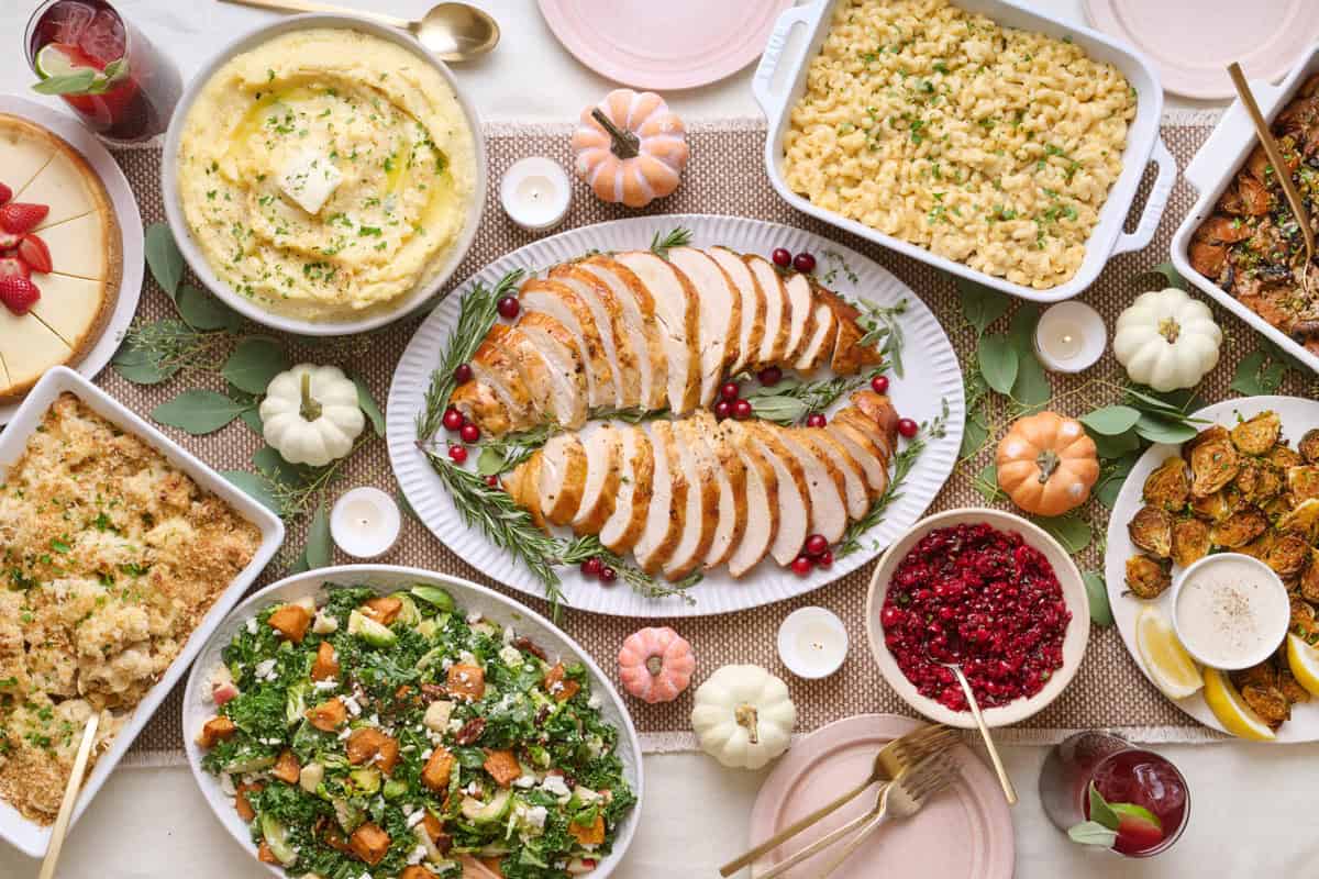 Feel Good Foodie's 2024 Thanksgiving Dinner menu recipes on table including air fryer turkey breast, mashed potatoes, mac and cheese, mushroom stuffing, brussel sprouts, fall harvest salad, cauliflower au gratin, cheesecake cranberry salsa, and pomegranate mocktail.