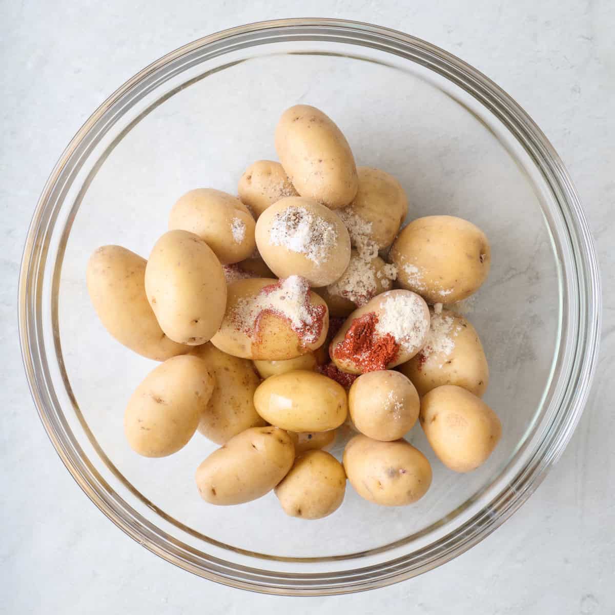 Potatoes, oil and spices in a bowl before tossing together.