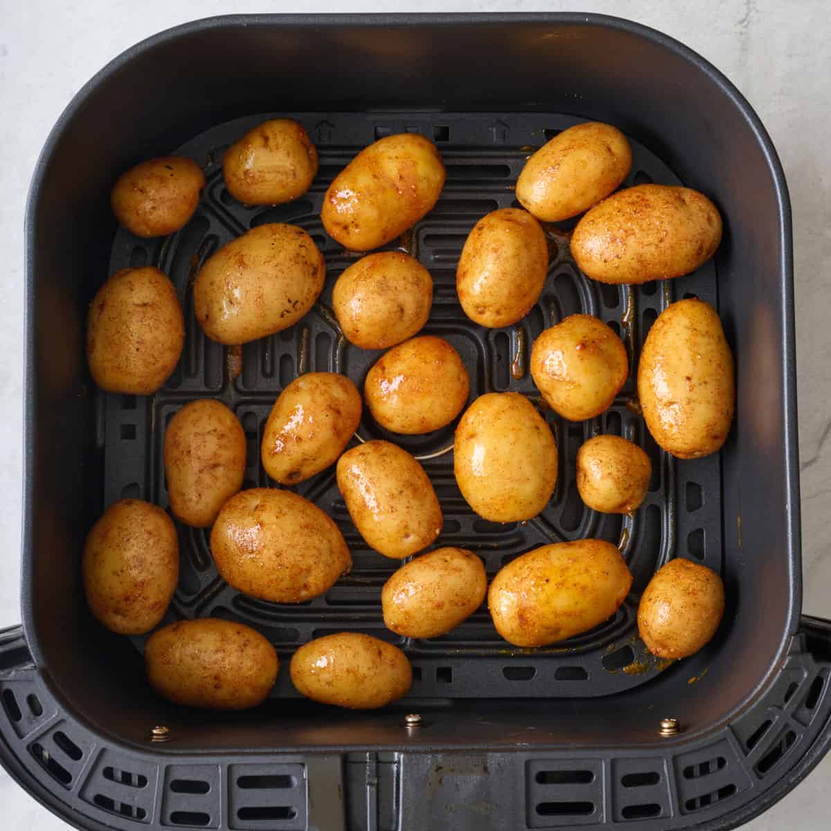 Seasoned small potatoes in an air fryer basket before cooking.