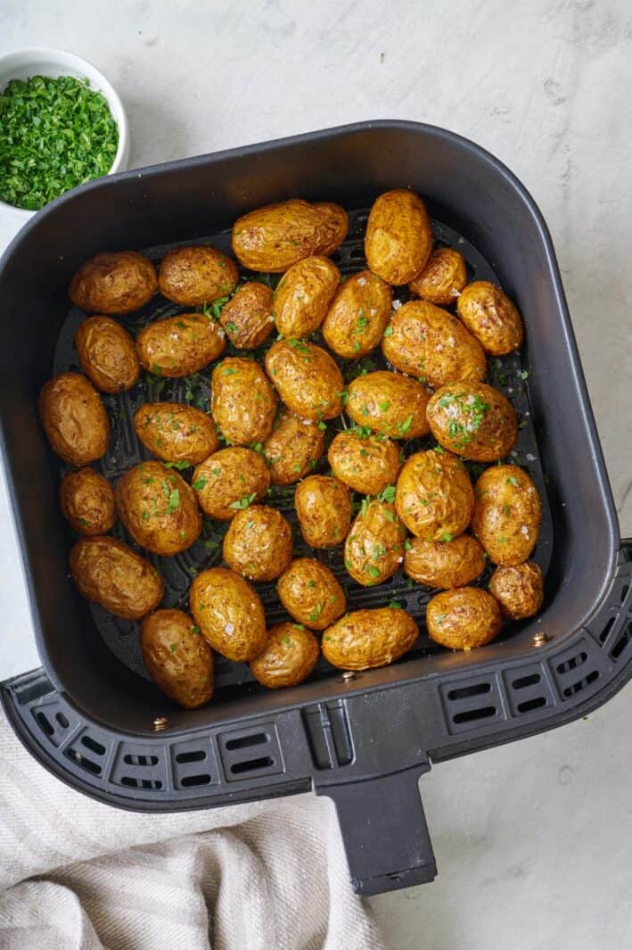 Seasoned air fryer baby potatoes in an air fryer basket garnished with flaky salt and fresh parsley.