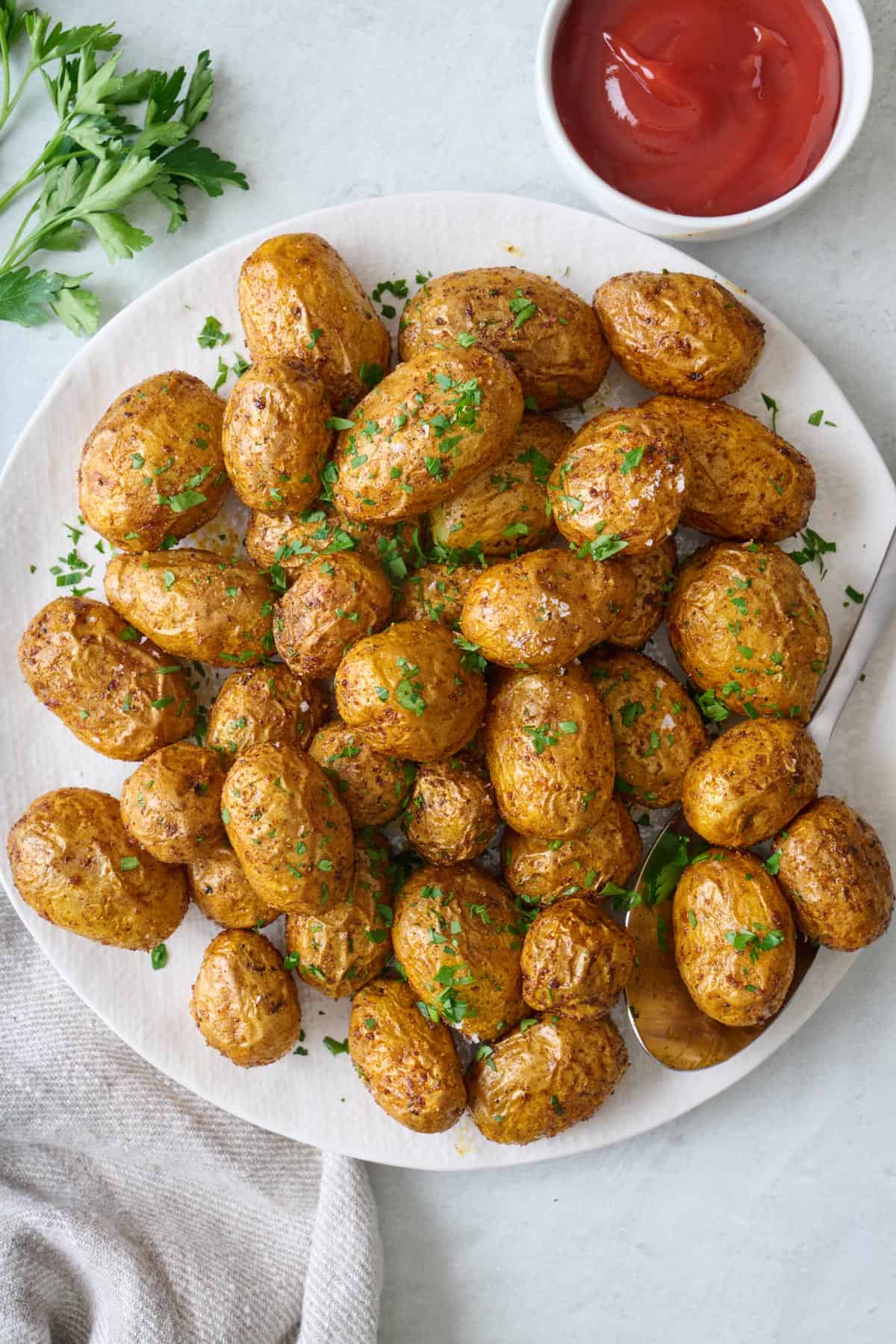 Crispy air fried baby potatoes on a plate garnished with flaky salt and chopped parsley.