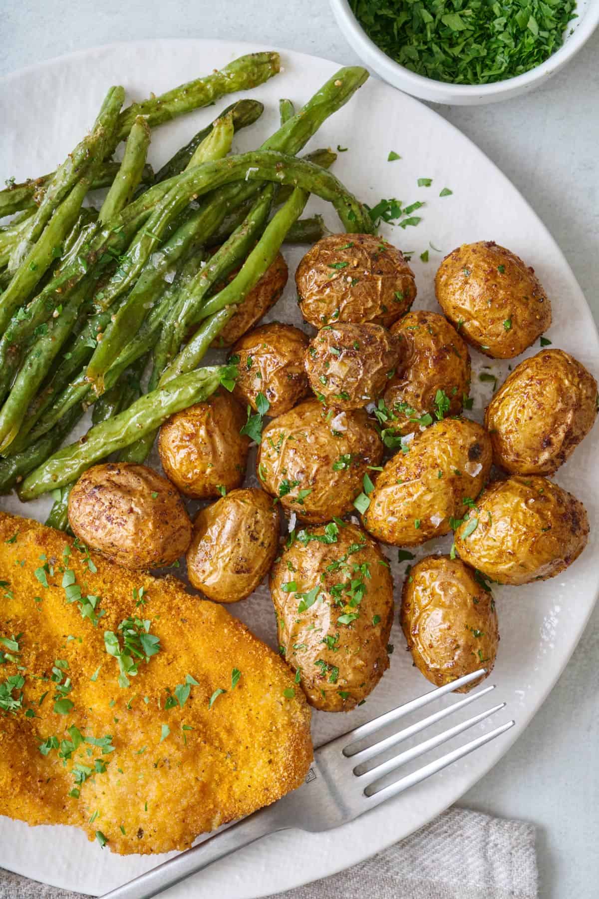 Air fryer baby potatoes on a plate with crispy chicken and green beans.