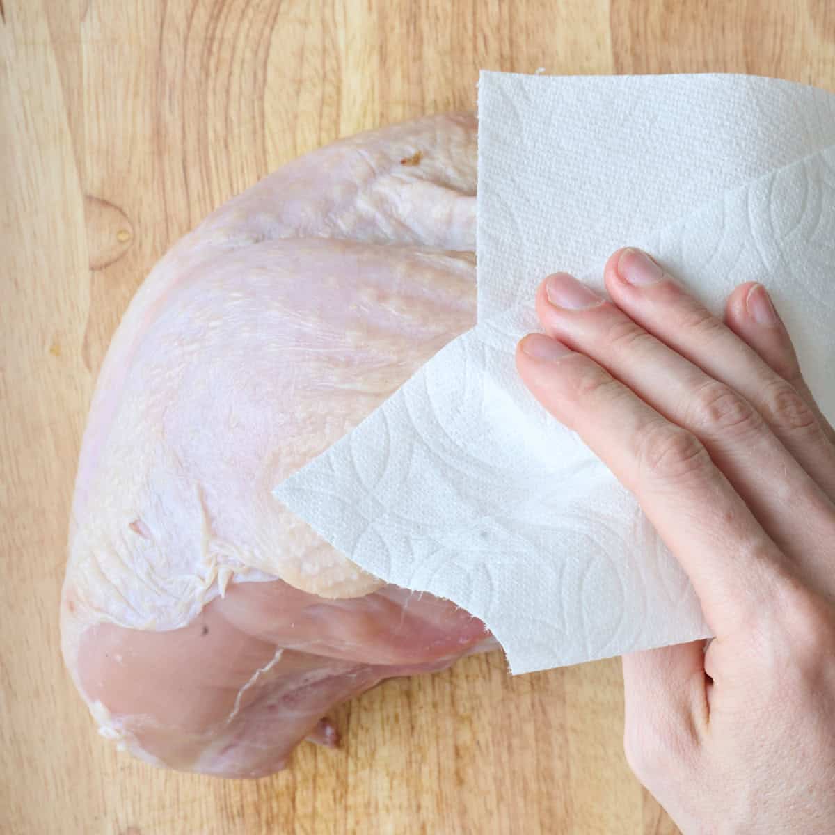 Patting turkey breast dry with a paper towel.