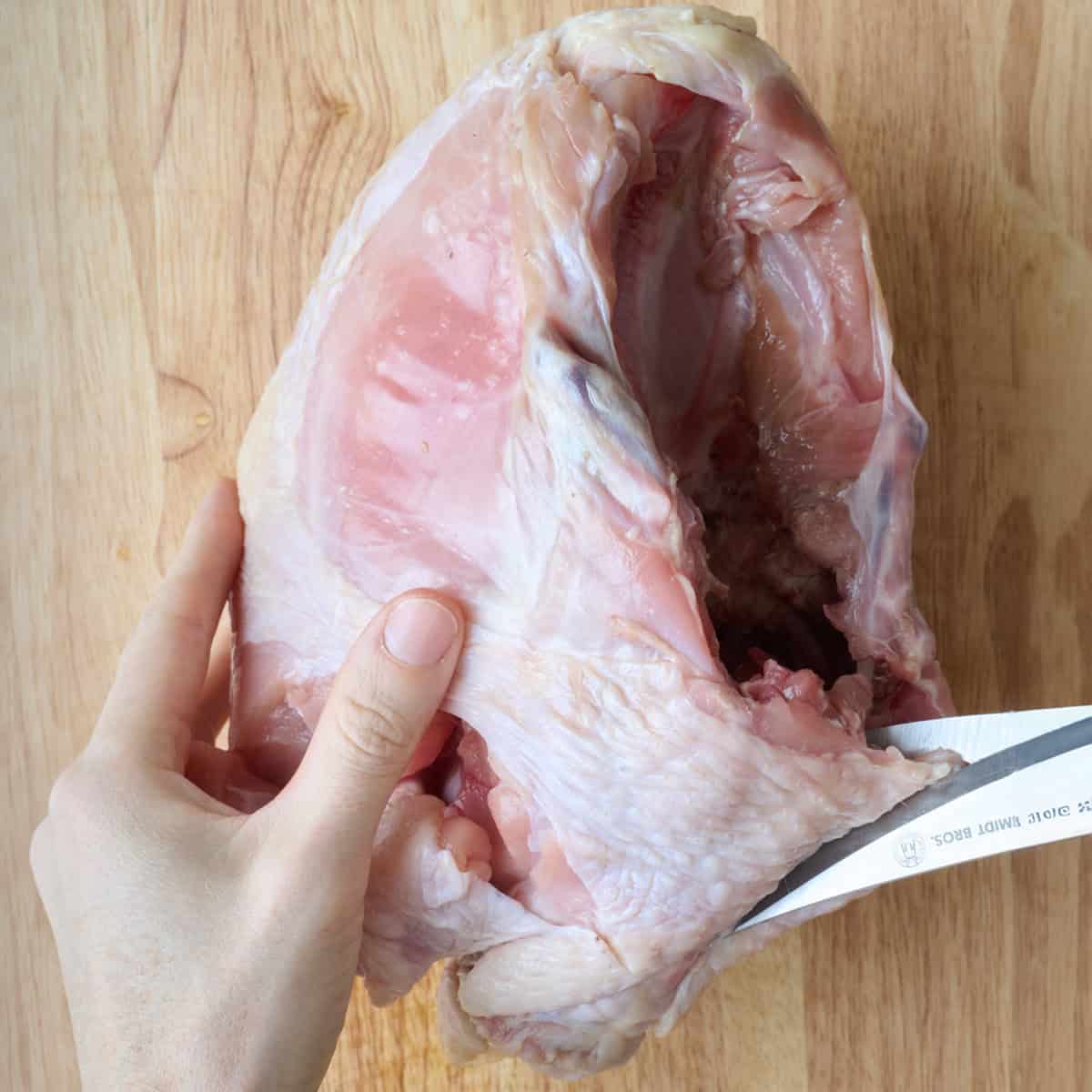 Kitchen shears cutting back of turkey breast.