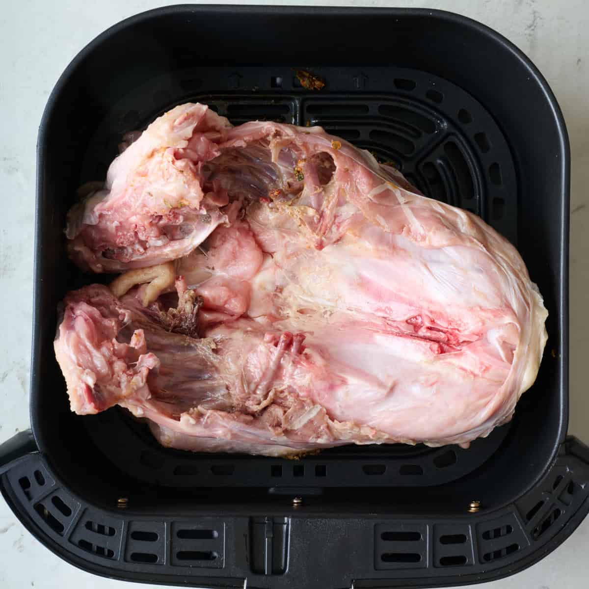 Seasoned turkey breast side down in a an air fryer basket.