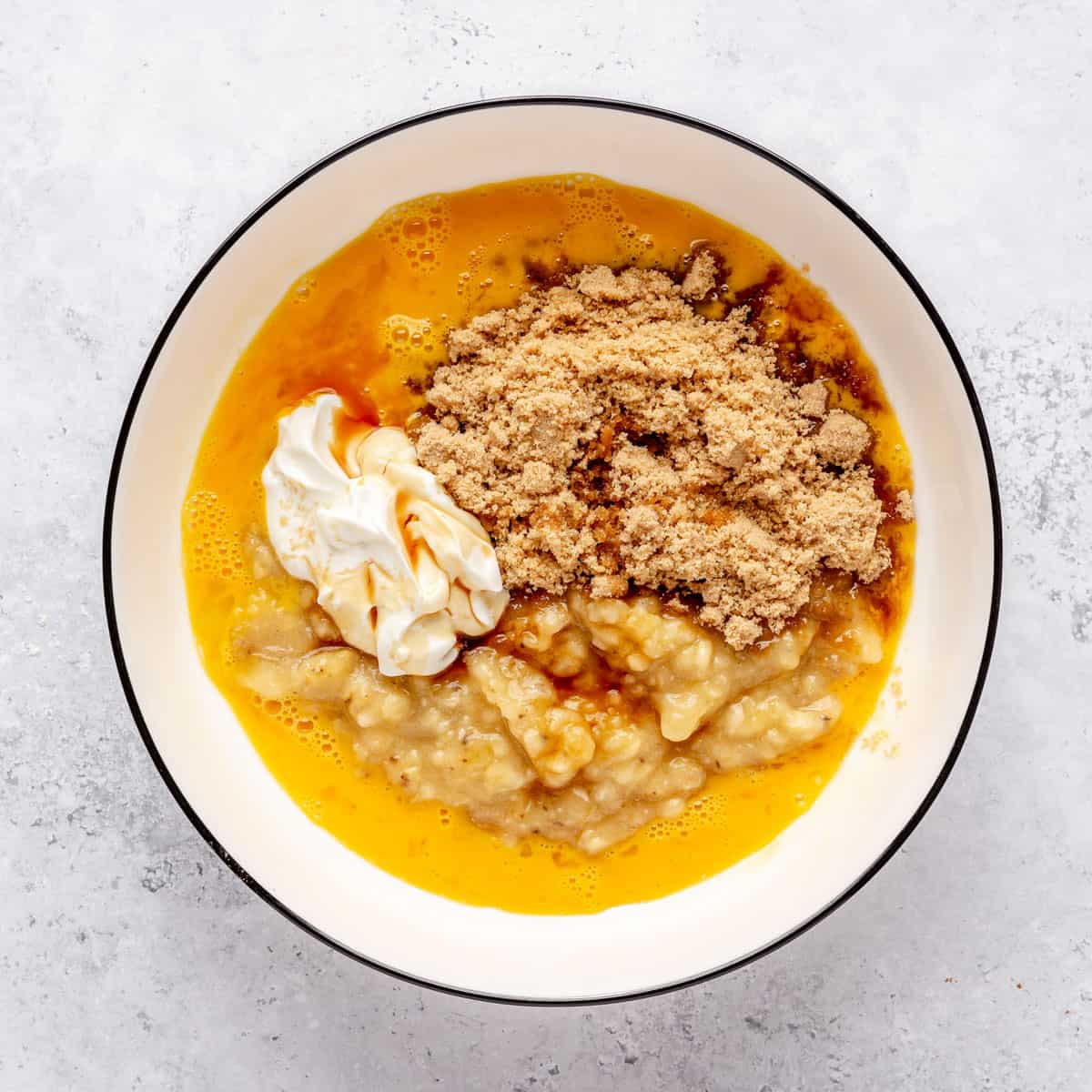 Eggs, mashed banans, yogurt, brown sugar and vanilla in a bowl.