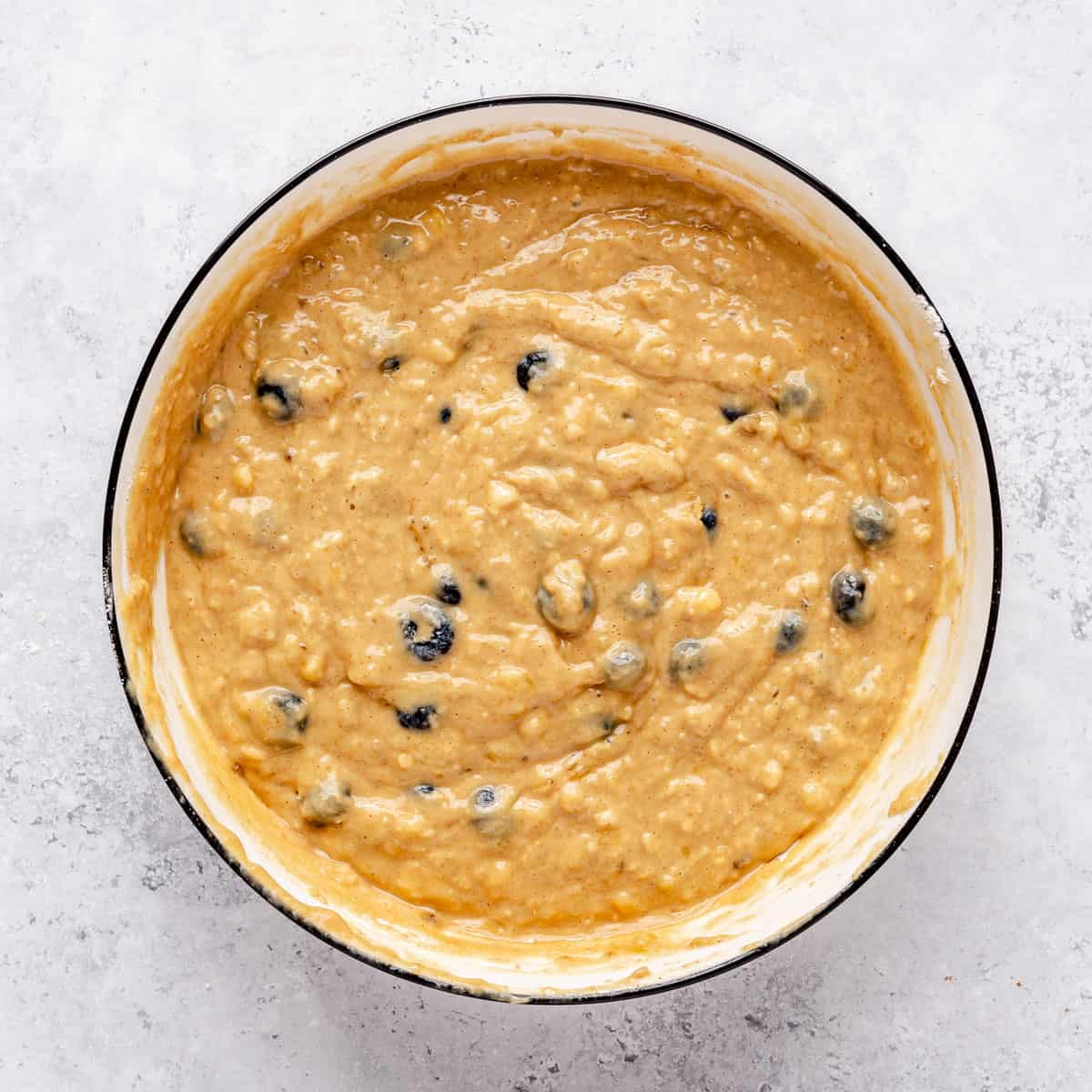 Blueberries folded into muffin batter in a bowl.