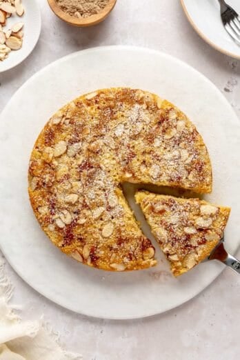 Cardamom cake on a round platter with a slice being removed.