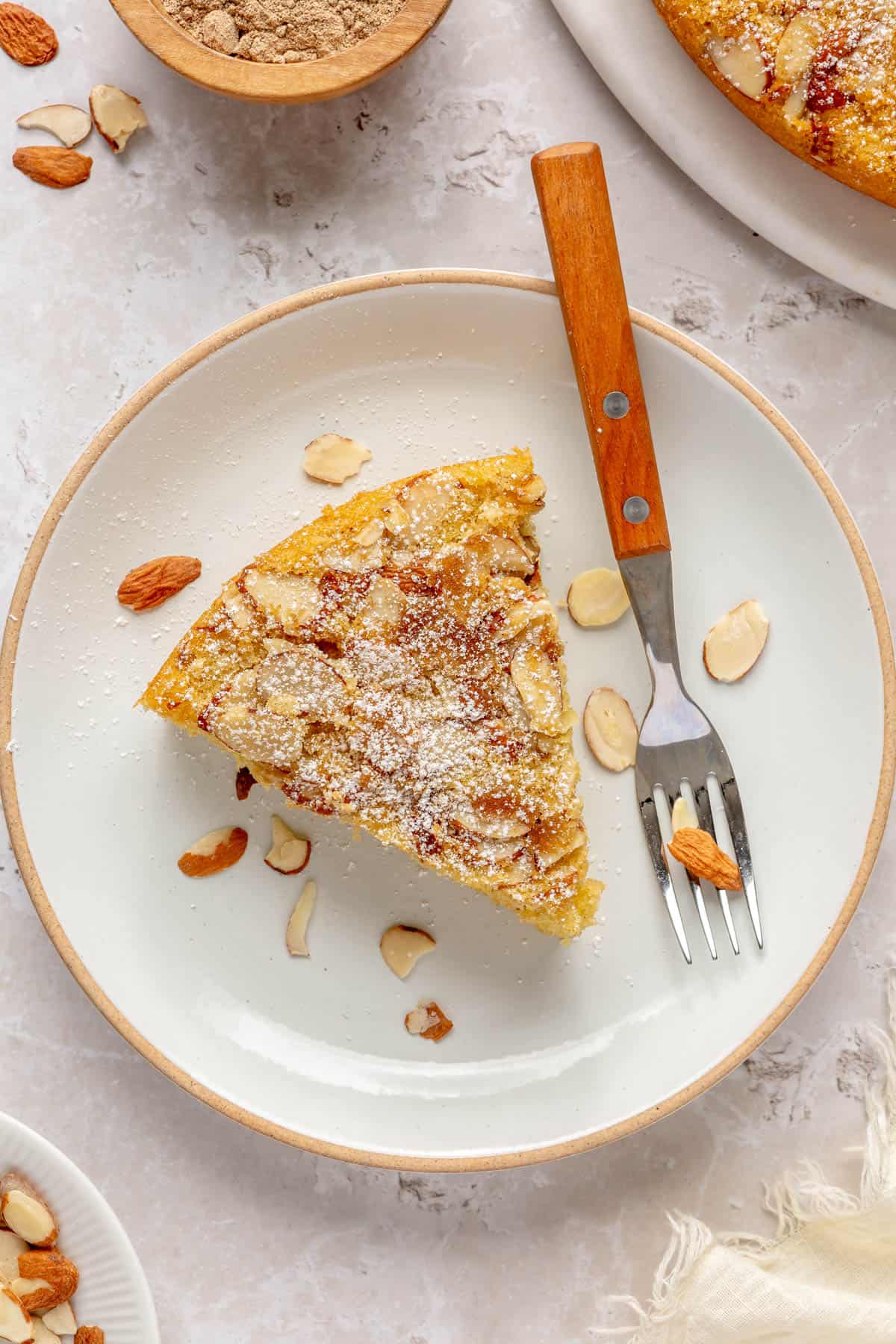 Slice of cardamom cake with almonds on a small plate with fork.