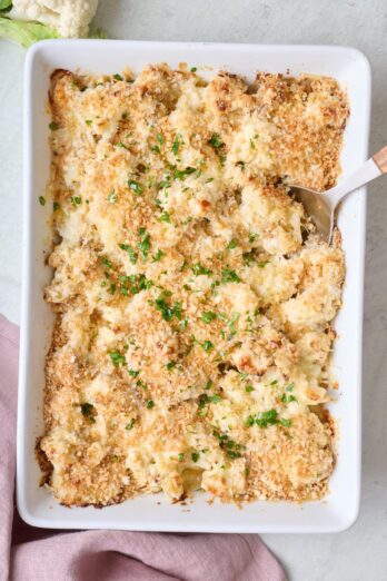 Cauliflower au gratin in a baking dish with a spoon dipped in.