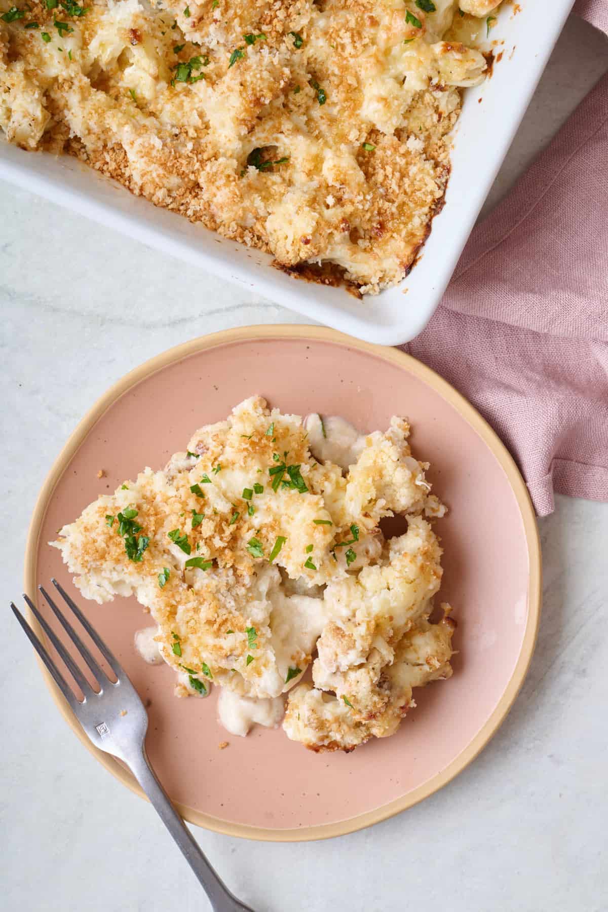 Serving of cauliflower au gratin on a plate with baking dish nearby.