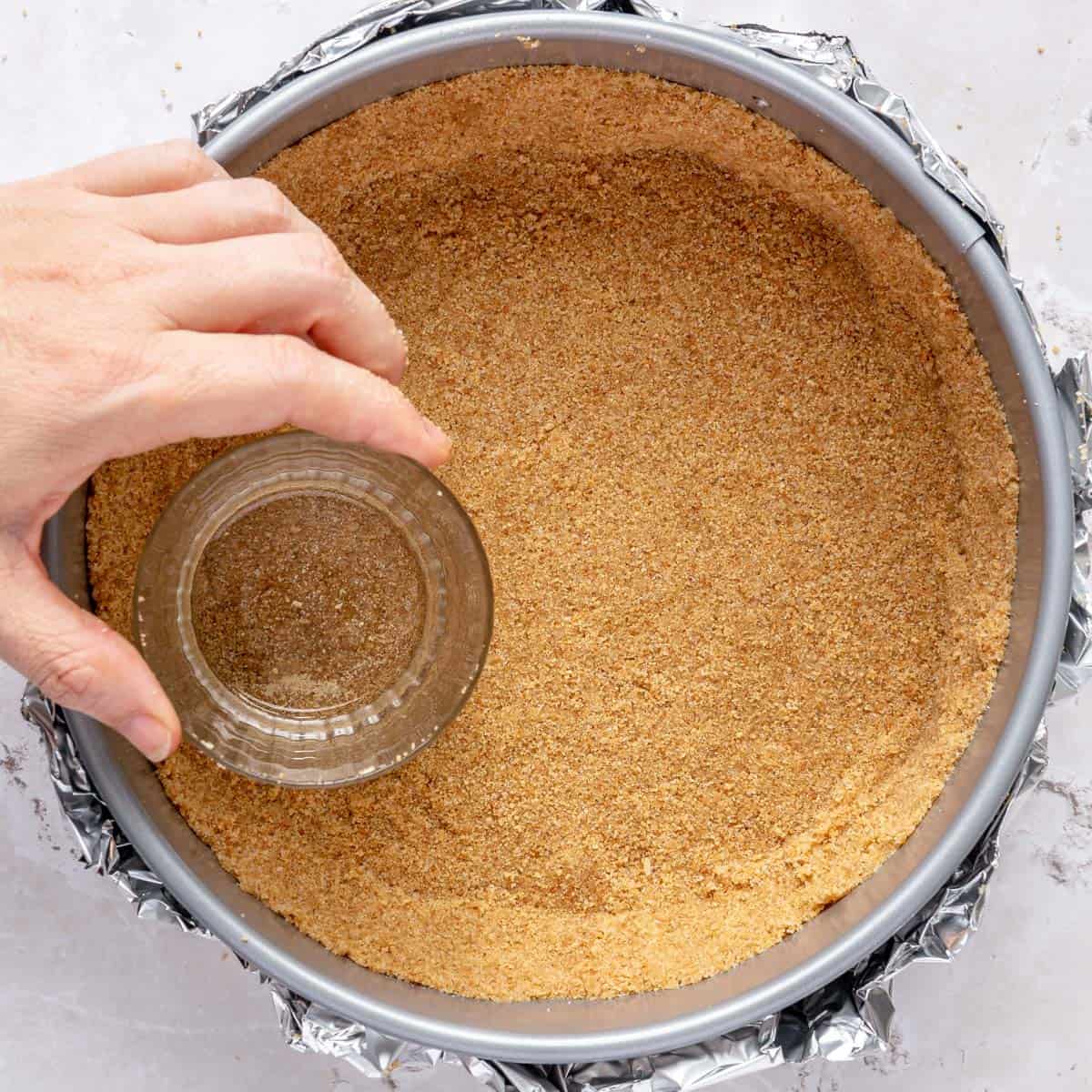 Pressing graham cracker crumbs into springform pan.