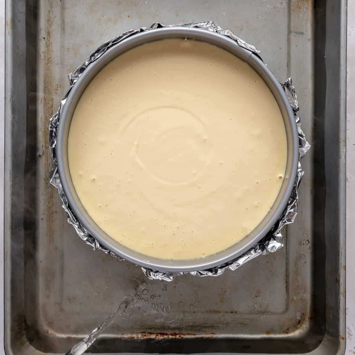 Cheesecake pan in a large roasting pan with water being poured in.