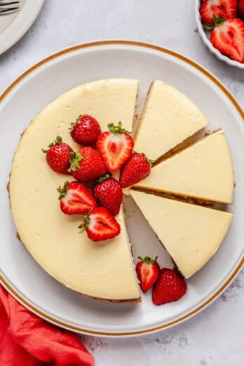 Cheesecake on a cake plate with a few slices with a slice removed, garnished with fresh strawberries.