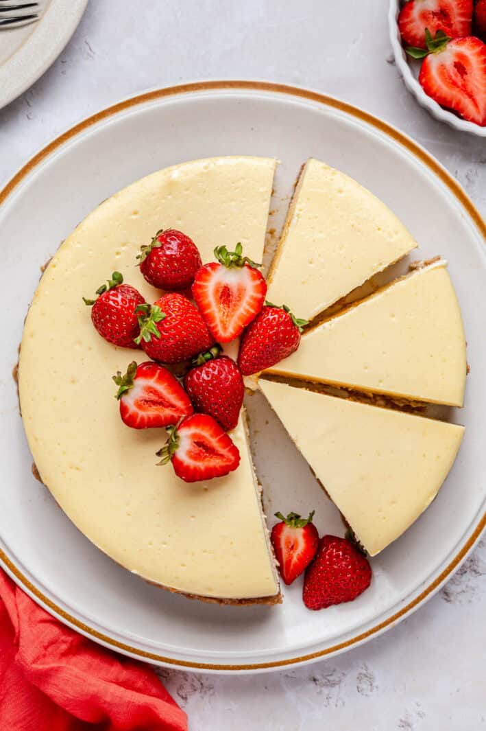 Cheesecake on a cake plate with a few slices with a slice removed, garnished with fresh strawberries.