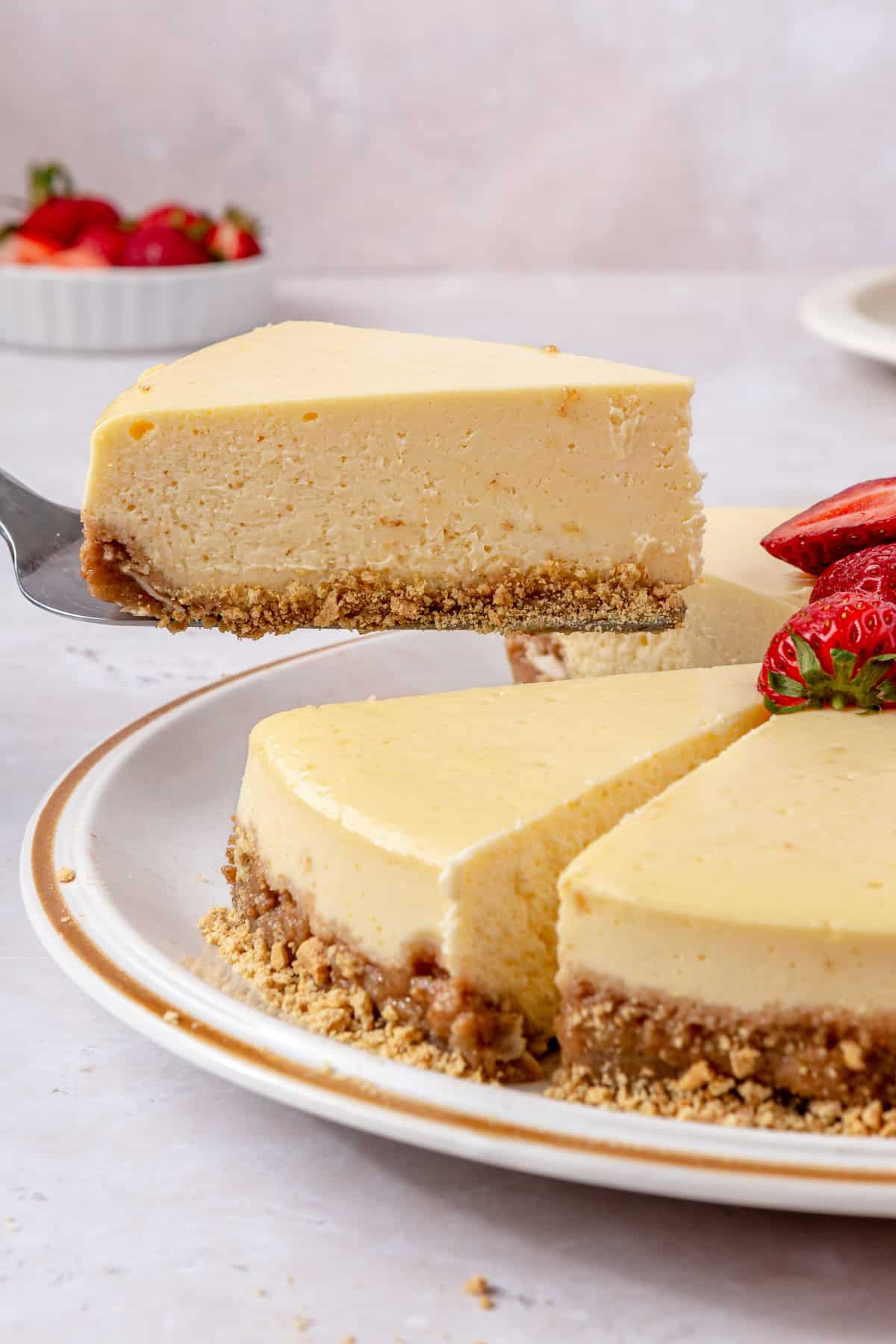 Cheesecake on a cake plate with a few slices cut and one slice being removed showing the side texture.