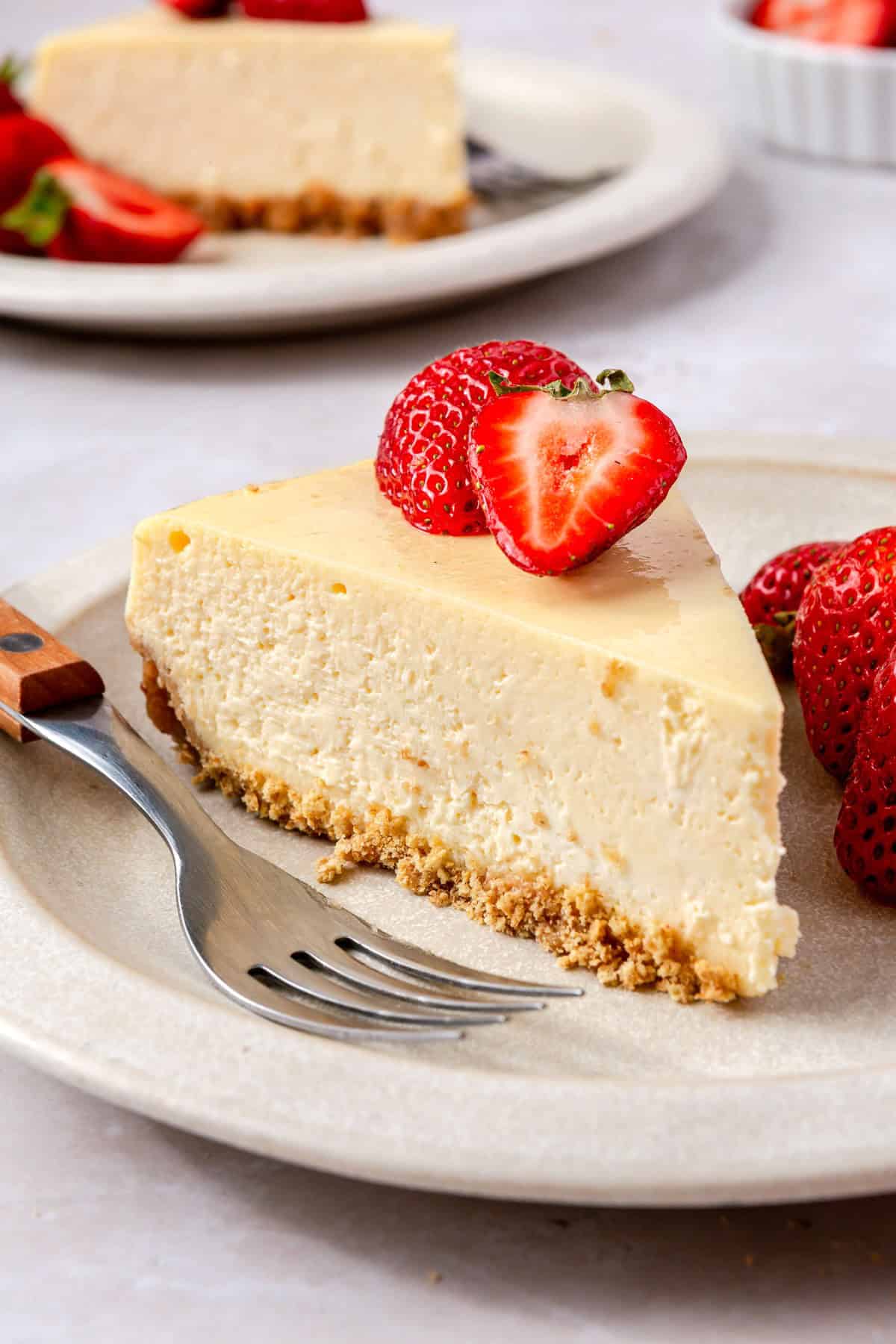 Two plates with a slice of cheesecake with fresh strawberries and forks on plate.