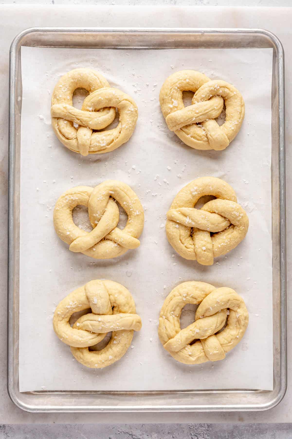 Pretzels on a parchment lined baking sheet sprinkled with coarse salt before baking.