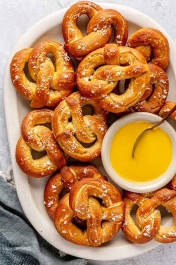 Easy soft pretzel recipe on a large platter with flaky salt and a small dish of sweet mustard sauce.