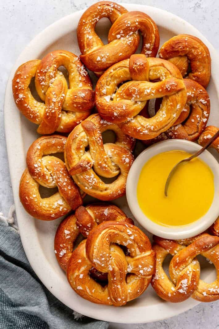 Easy soft pretzel recipe on a large platter with flaky salt and a small dish of sweet mustard sauce.