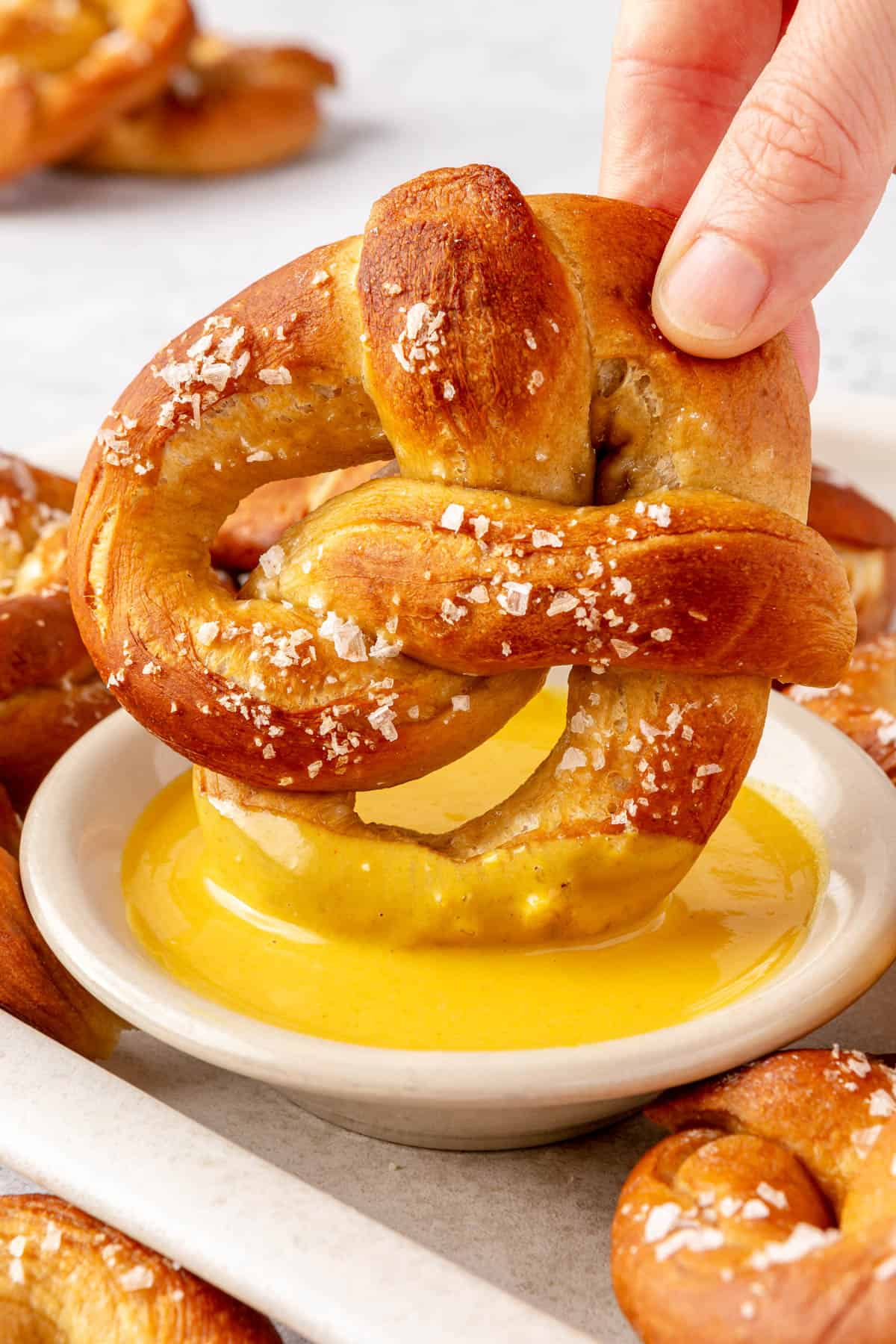 Dipping a soft pretzel with flaky salt into a small dish of mustard sauce.