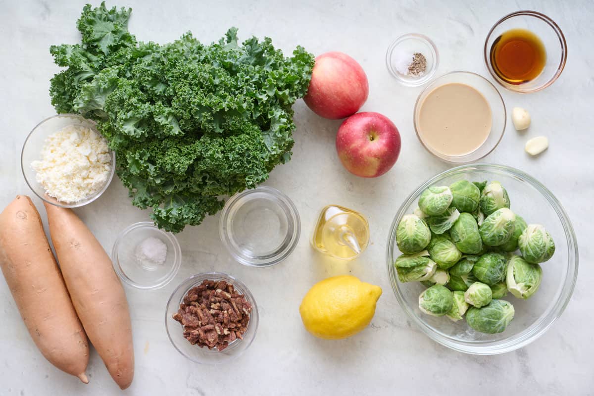 Ingredients for recipe before prepping: sweet potatoes, kale, feta, salt, water, candied pecans, oil, lemon, apples, salt and pepper, tahini. maple syrup, garlic cloves, and brussels sprouts.