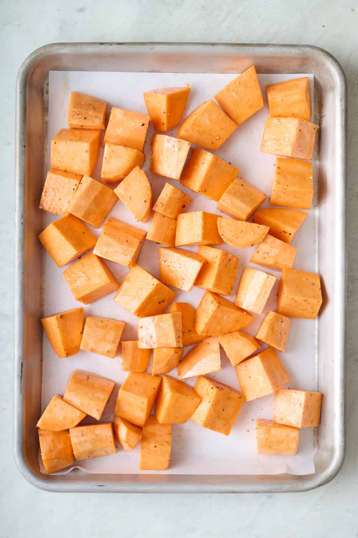 Sweet potato chunks on a baking sheet, seasoned with oil, salt and pepper before roasting.