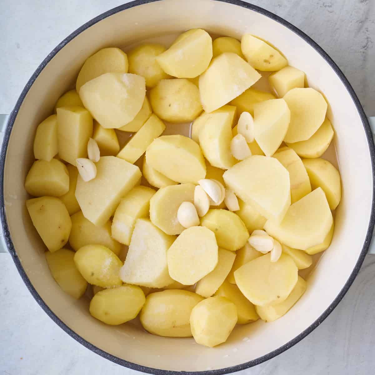 Peeled potato chunks and whole garlic cloves in a pot with water.