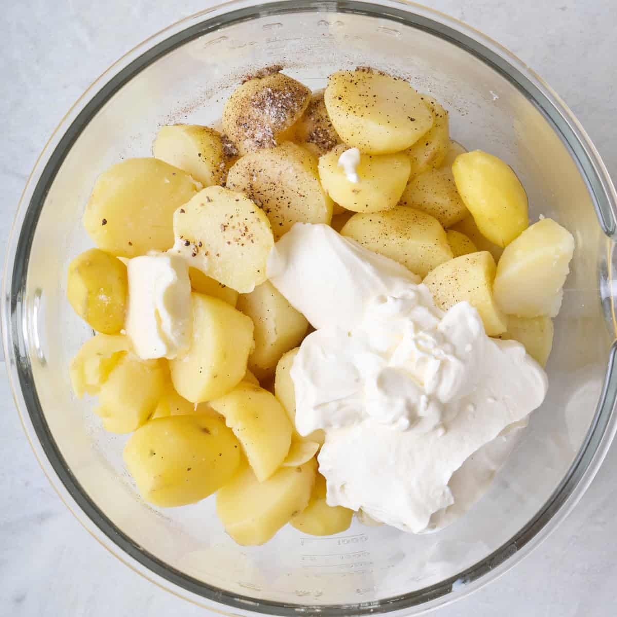 Cooked potatoes and garlic in a bowl with salt, pepper, broth, and sour cream.