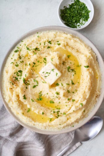 Healthy mashed potatoes in a serving bowl garnished with a pat of butter and chopped parsley.