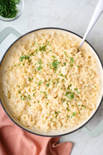 Mac & cheese in pot garnished with fresh ground black pepper and light sprinkling of chopped parsley, and a spoon dipped inside