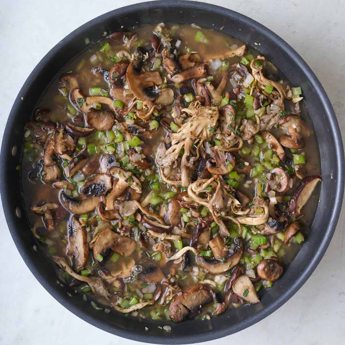 Broth adding to mushrooms in skillet.