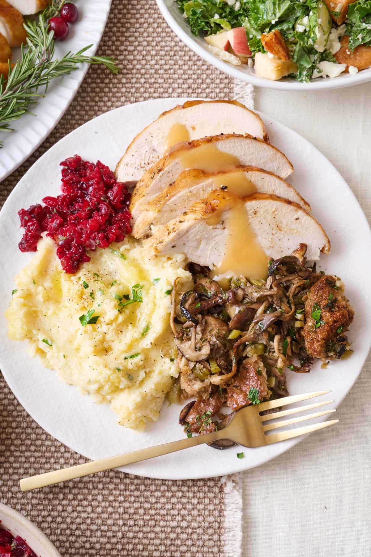 A plate with mushroom stuffing, mashed potatoes, cranberry sauce, and sliced turkey with gravy.