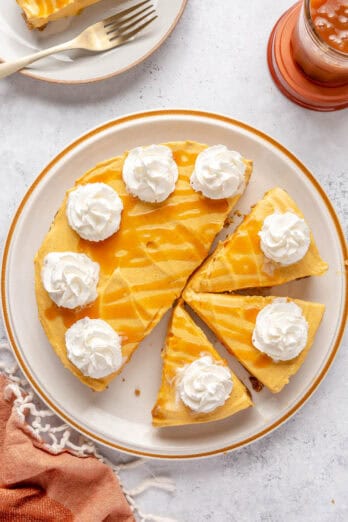 Pumpkin cheesecake with whipped cream rosettes around the edges and some type of caramel sauce, 3 slices cut and slightly pulled away and 1 on a small plate nearby.