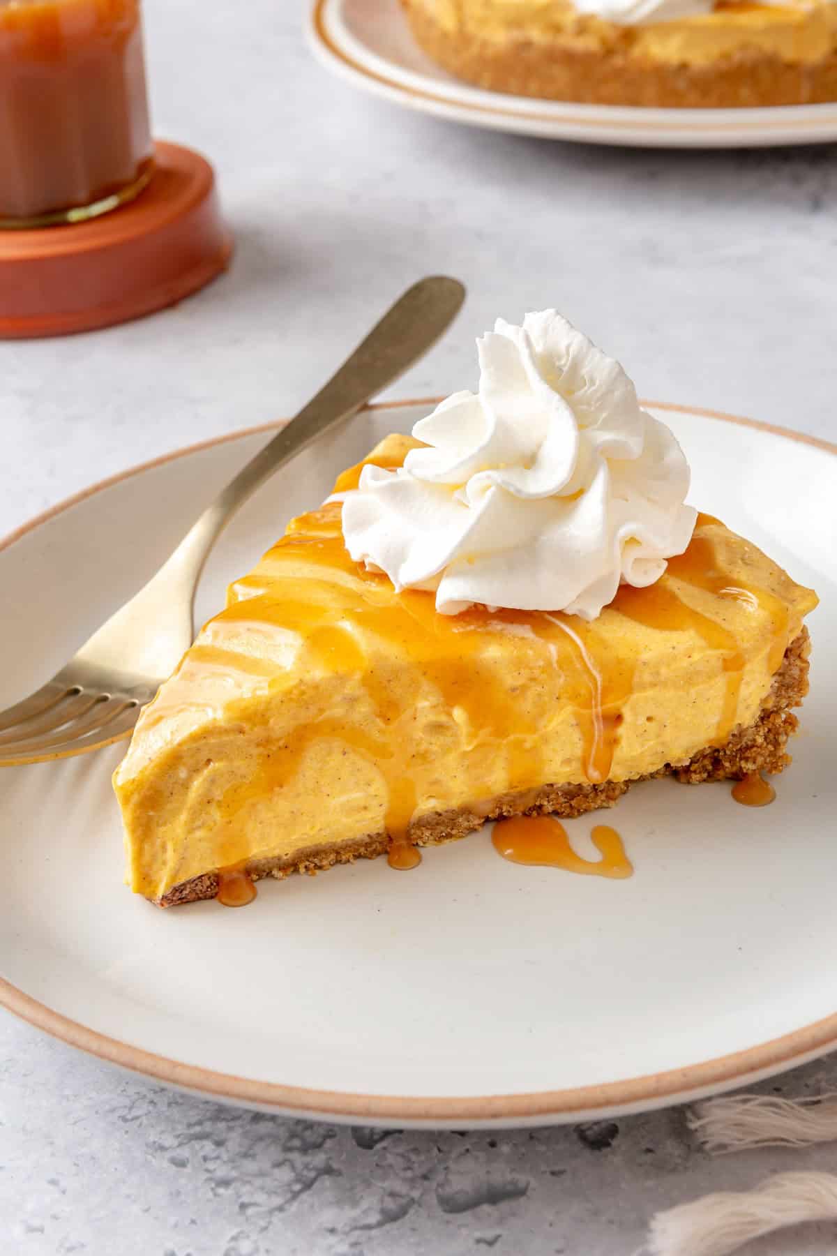 Easy no bake pumpkin cheesecake slice on a plate topped with caramel and whipped cream.