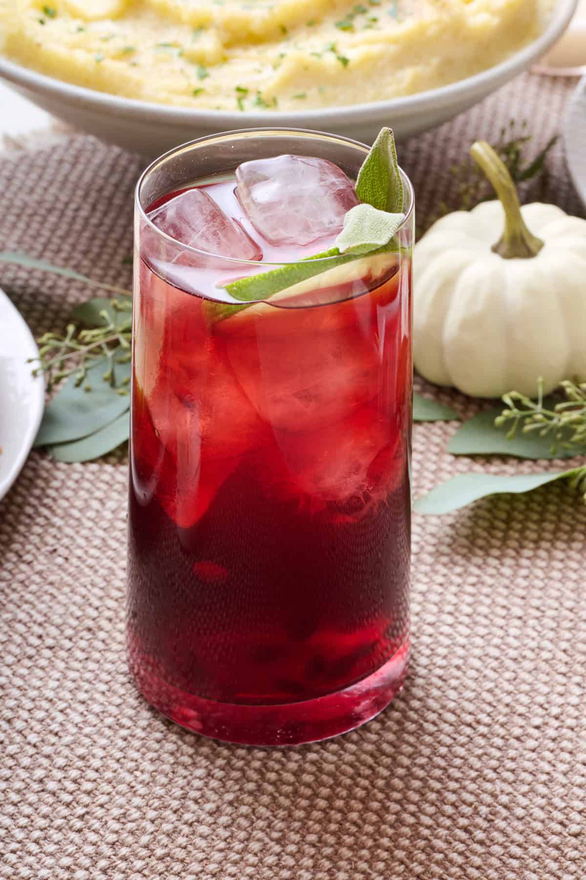 Pomegranate mocktail in a tall glass with ice and fresh sage garnish.