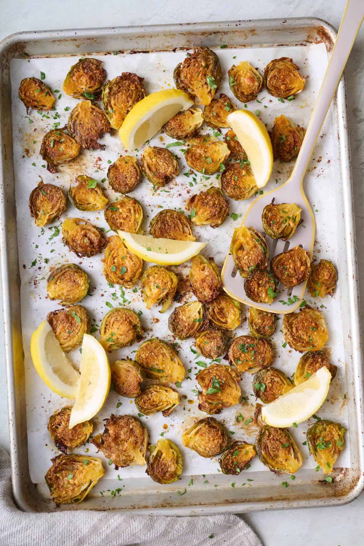 Smashed brussel sprouts on a sheet pan with lemon wedges.