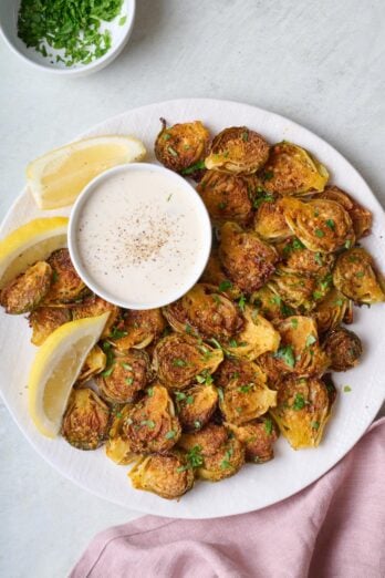 Smashed brussel sprouts on a plate with ranch sauce for dipping.